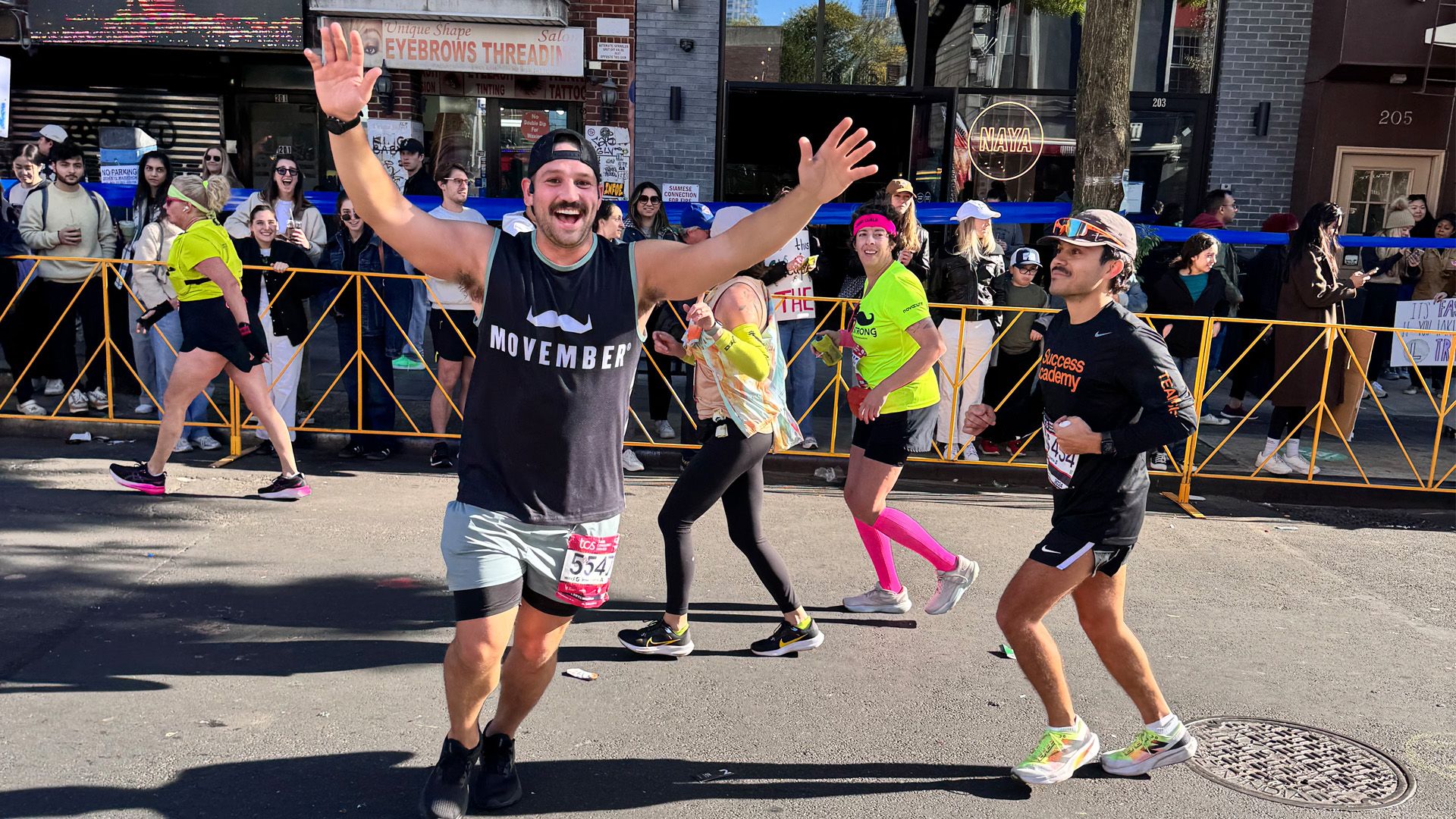 Movember runner competing in New York City Marathon, triumphantly running past camera.