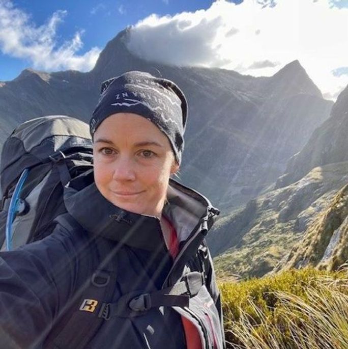 Photo of a woman in climbing attire, posing in front of a stunning mountain view.