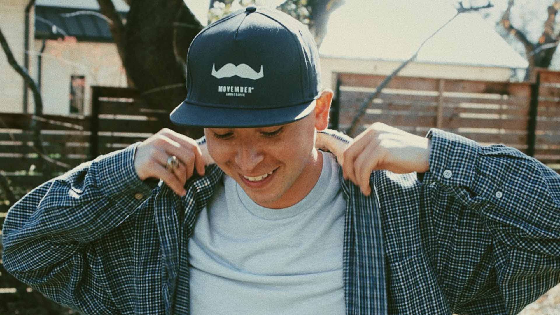 Young man smiling to camera, wearing a Movember-branded cap.