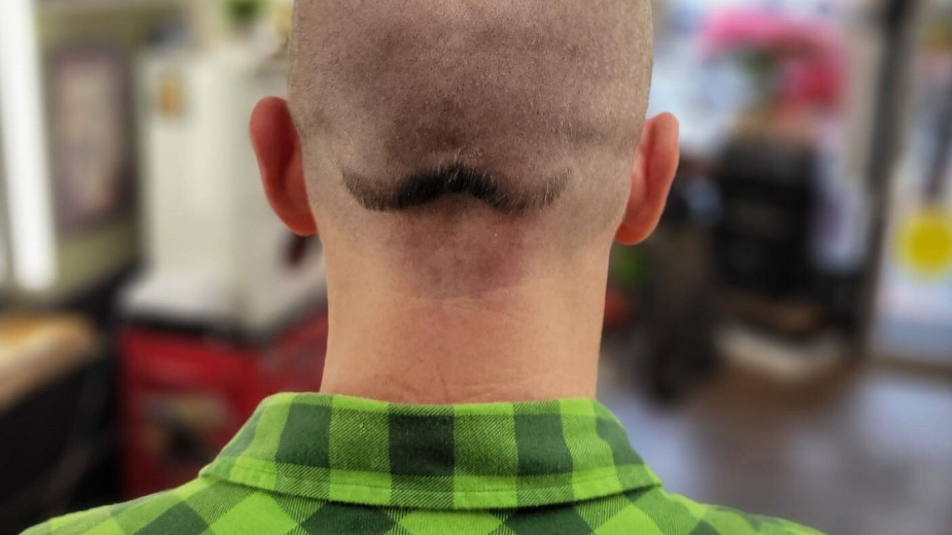A moustache shaved into the back of a bald man's head.