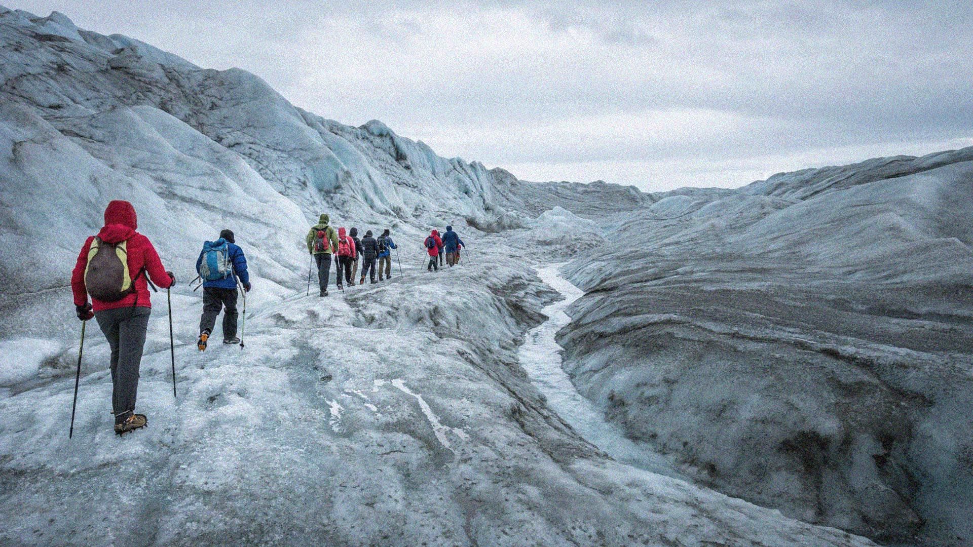 A column of hikers in cold-weather gear, traversing a frozen glacial valley in Greenland.