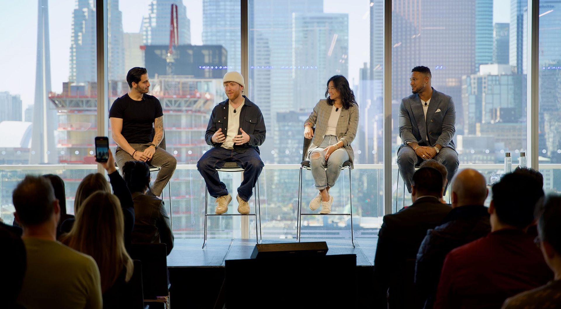 A mixed panel of experts sits on a stage in front of the Toronto skyline 