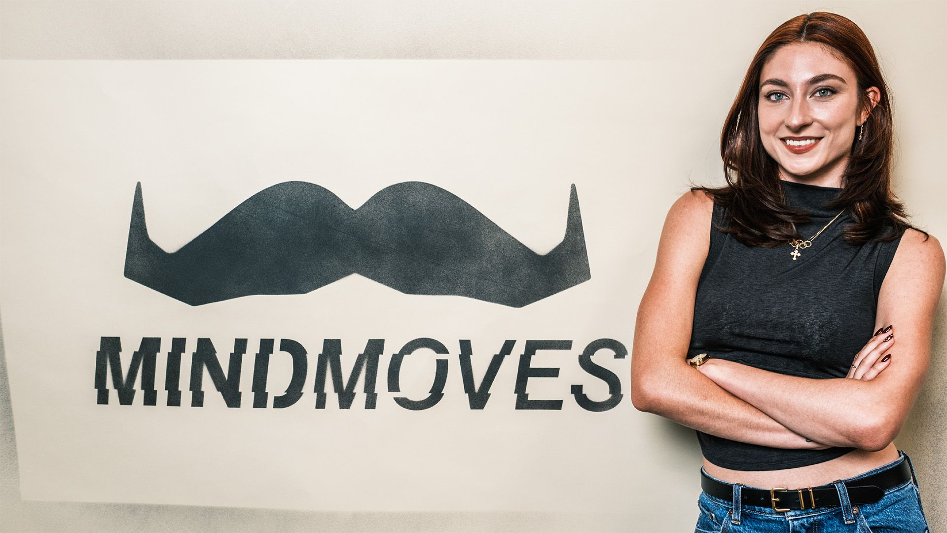 Photo of an athletic young woman posing in front of a sign that says "Mind Moves".