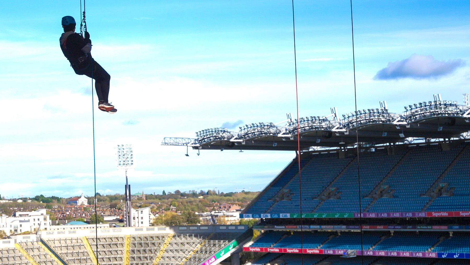 Photo of person abseiling down rope, with Croke Park stadium visible behind.