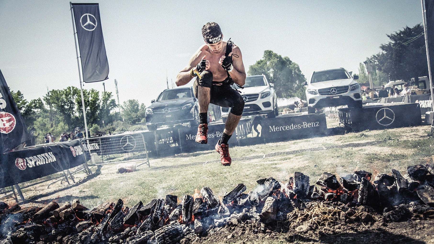 Photo of Spartan Races competitor, leaping over an obstacle of burning wooden logs.