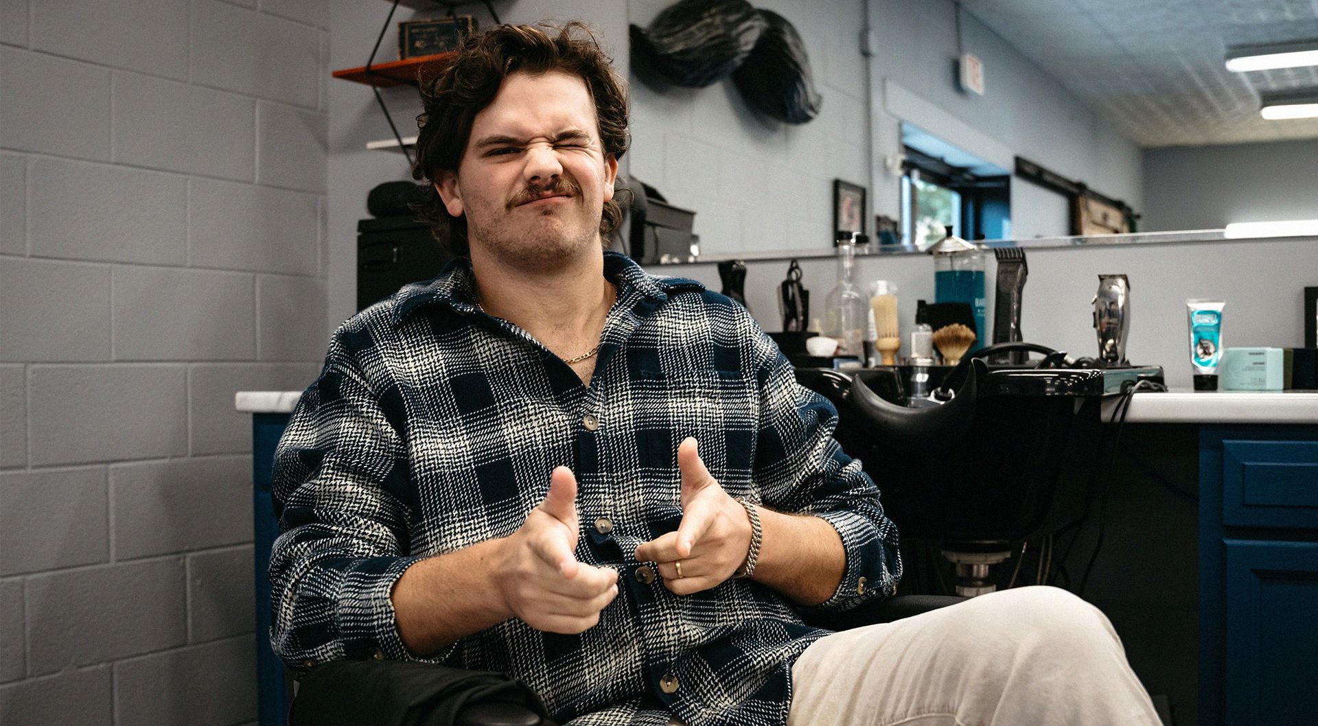 Man scrunching up his face in a barber chair and pointing finger guns playfully at the camera 