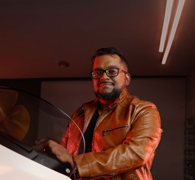 Photo of man in leather jacket, seated on a motorcycle.