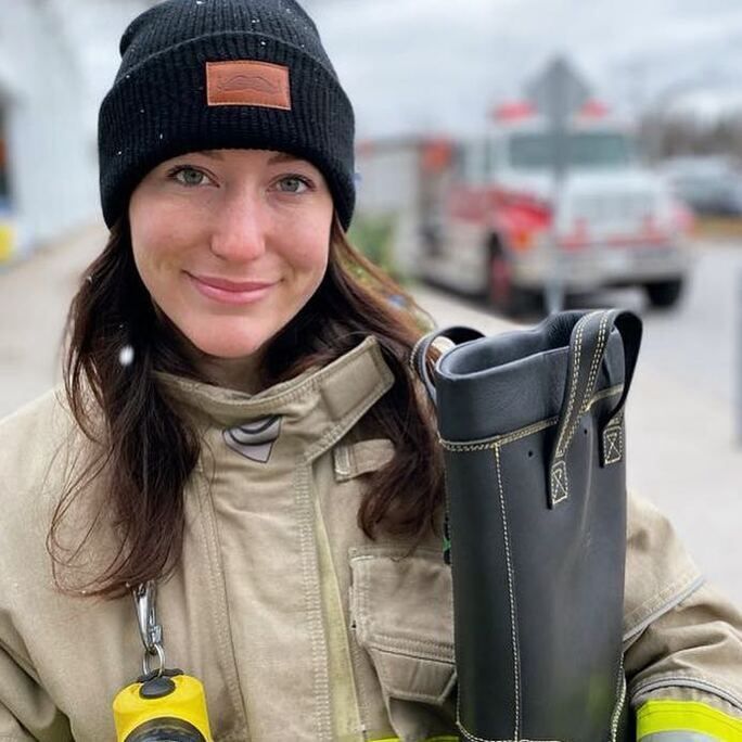 Young woman looking to camera, wearing firefighting bunker gear.