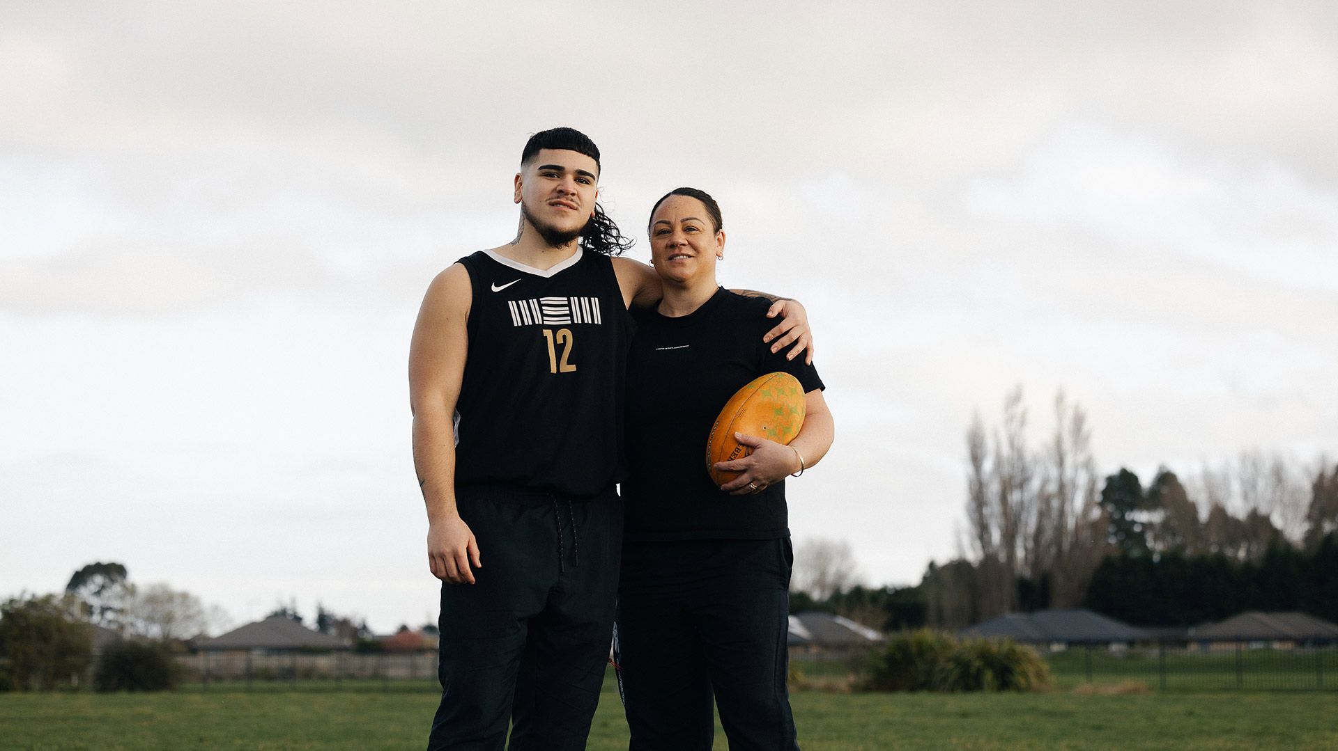 Photo of woman and her son looking to camera and holding a rugby ball.