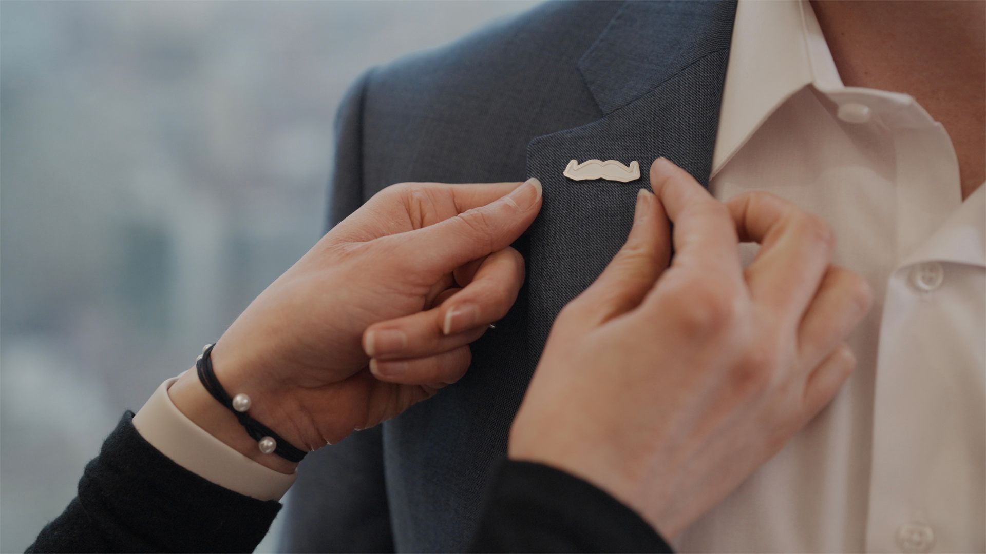 Movember moustache pin being pinned to a suit lapel