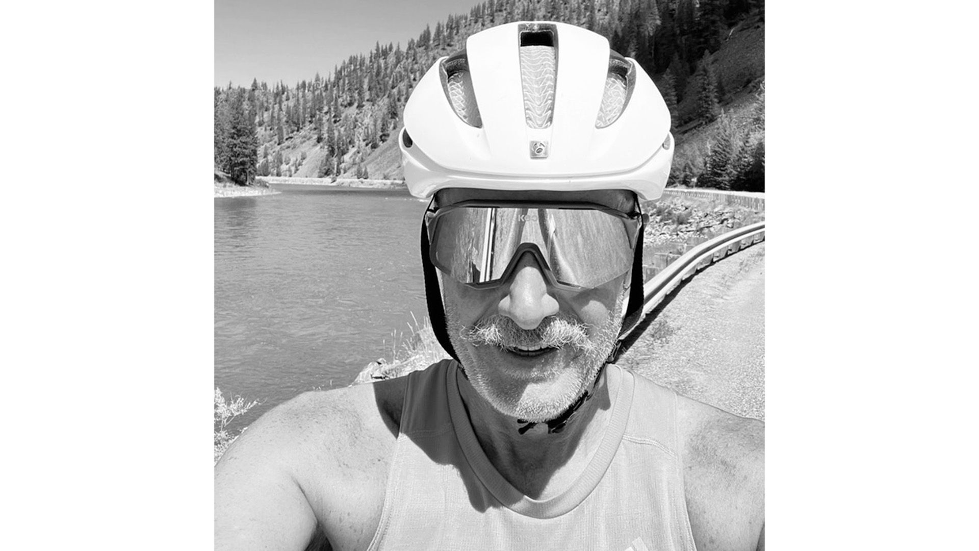 Portrait black and white photo of a man looking to camera, decked in full bike riding gear.