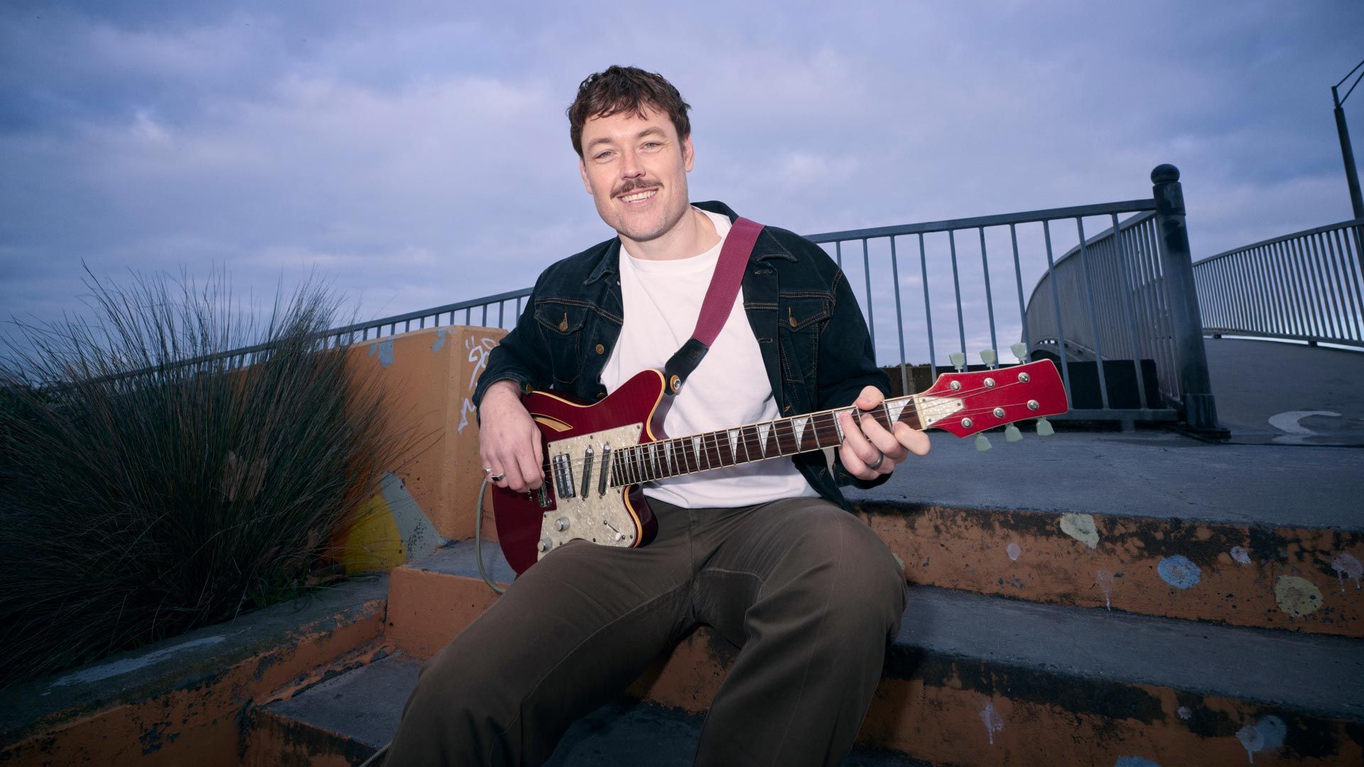Photo of young man strumming an electric guitar in public.