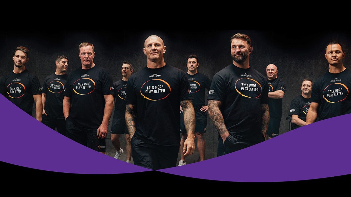 Group of rugby stars looking to camera. They wear branded tops that say: "Talk more. Play better."