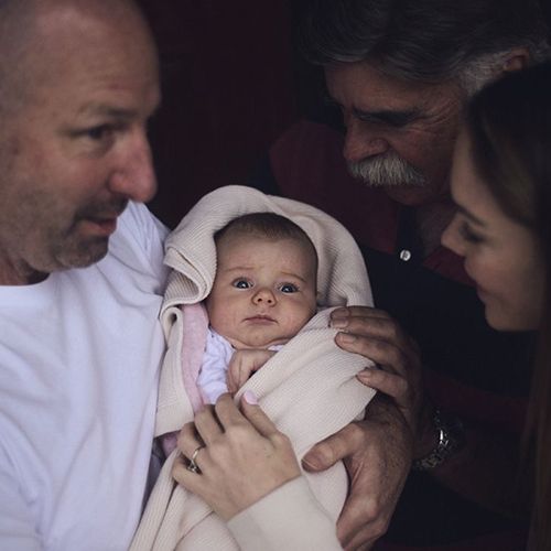 Photo of a father lovingly smiling at an infant, surrounded by family.