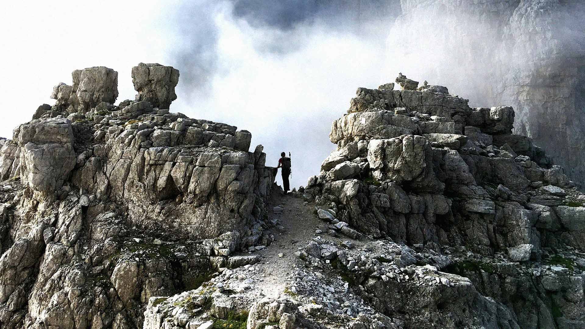 Photo of a mountain-top, with a hiker visible at its peak in the distance.