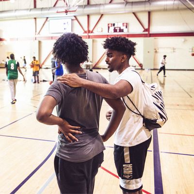 A photo of two adolescent men standing arm-in-arm at a basketball court.