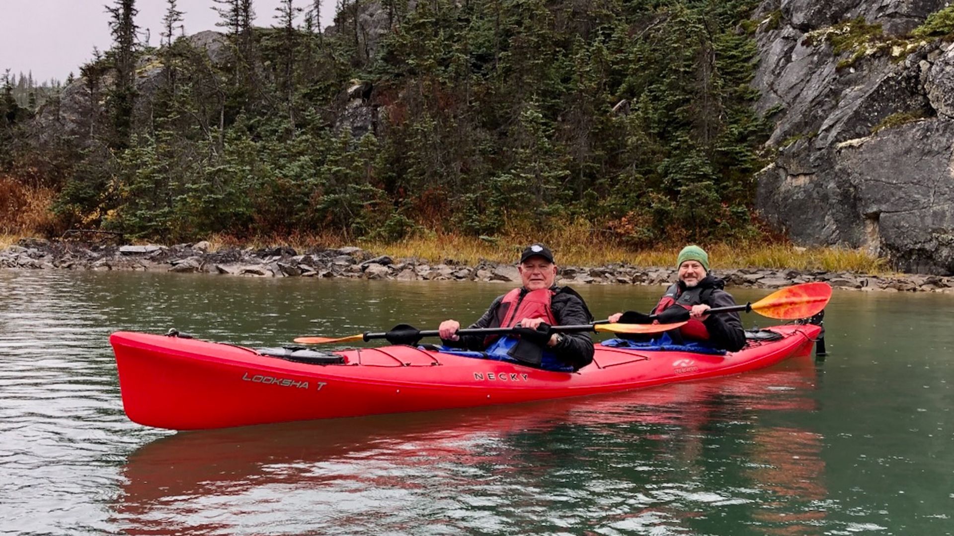 Adult son and father smile from a tandem kayak in Alaska