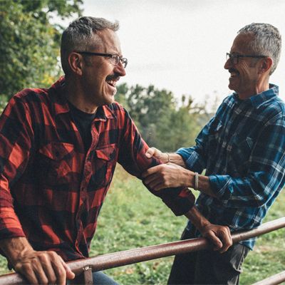 Two brothers laughing in conversation on a rural property. 
