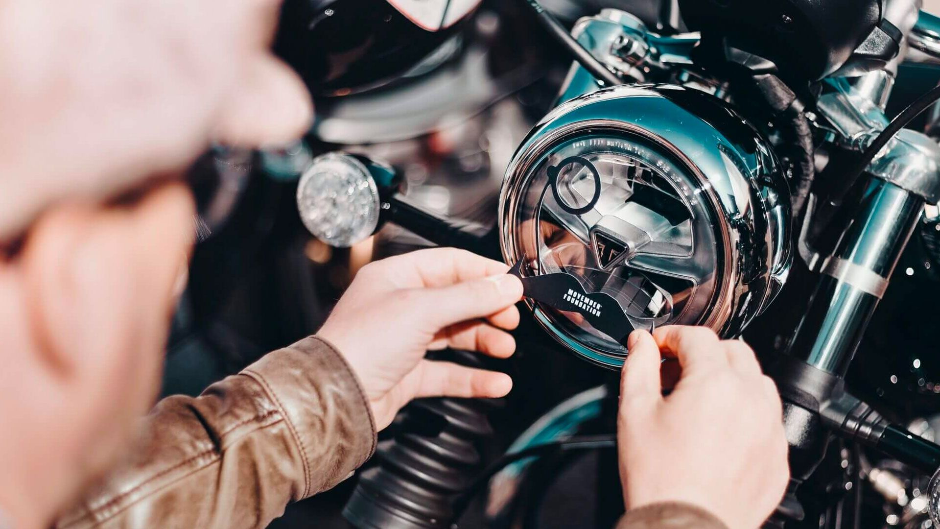 A DGR rider placing a moustache-shaped Movember sticker on their motorcycle headlight.