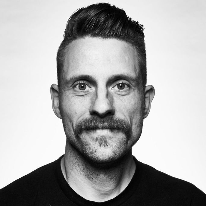 Black and white photo of dashing young man, donning an impressive moustache, looking to camera.