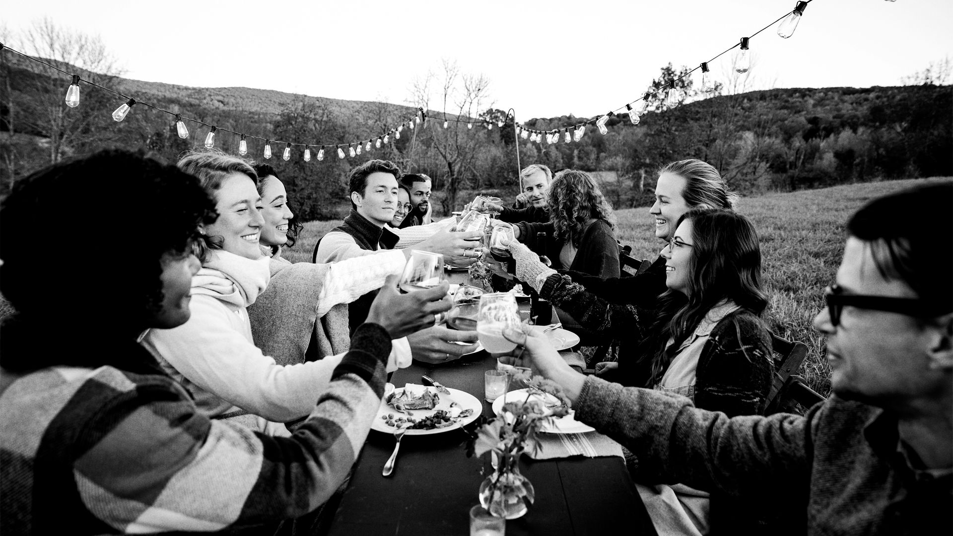 A group of friends and family sit around a long table outside, cheers-ing one another